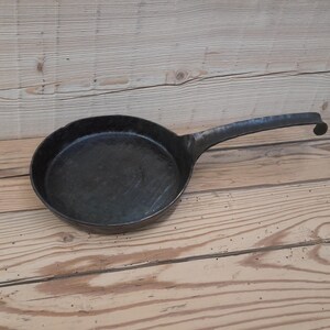 May include: A black cast iron skillet with a long handle. The skillet is sitting on a wooden surface.