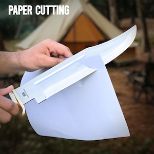 May include: A large, silver knife with a black handle and gold accents is cutting through a sheet of paper. The text "PAPER CUTTING" is displayed at the top of the image. The knife has the text "JD Delta Knives" on the blade.