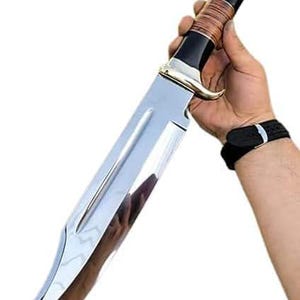 May include: A large, polished stainless steel knife with a curved blade. The handle is black with a brown wrapped section and a silver bolster and pommel. The knife is held against a white background.
