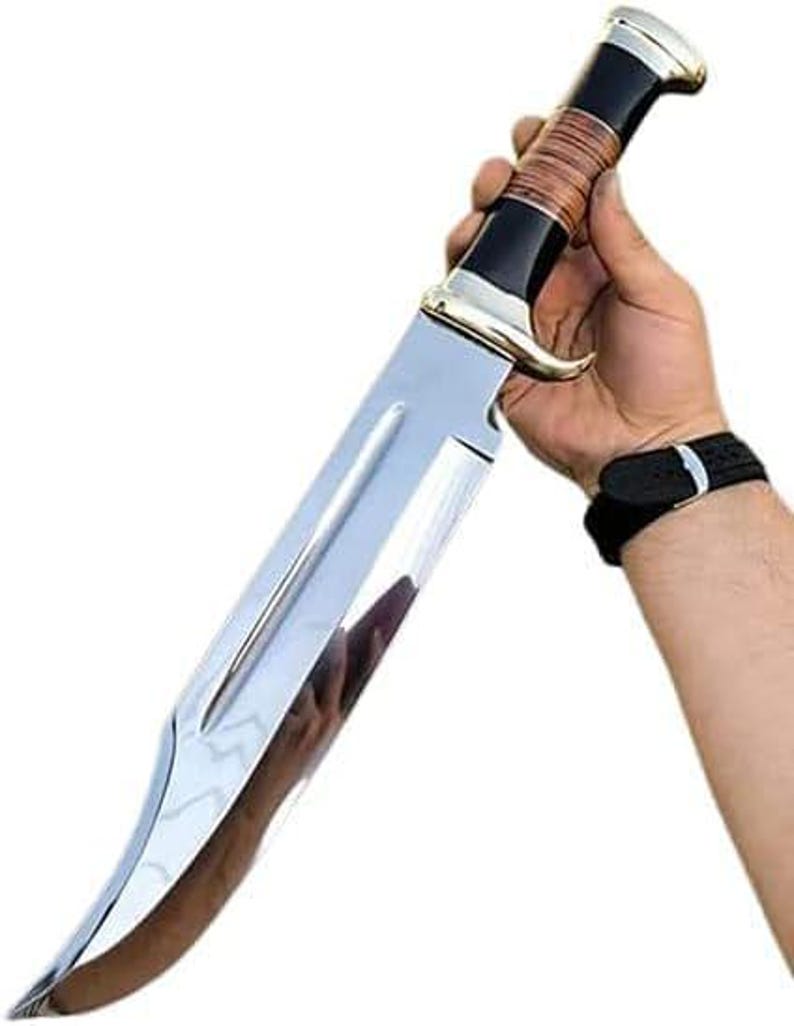May include: A large, polished stainless steel knife with a curved blade. The handle is black with a brown wrapped section and a silver bolster and pommel. The knife is held against a white background.