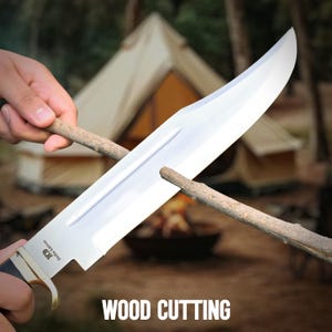 May include: A large, shiny silver knife with a black handle is being used to sharpen a wooden stick. The text "WOOD CUTTING" is displayed at the bottom of the image. A tent and campfire are in the background.