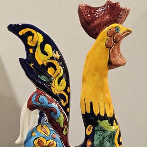 May include: A large, colorful ceramic rooster figurine. The rooster features a yellow body, a red comb, and a blue and yellow patterned tail. The base is decorated with blue and white floral designs.