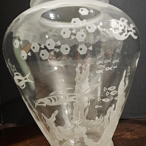 May include: A clear glass vase featuring a frosted finish on the rim and base. The body of the vase is decorated with etched, frosted designs of various fish, aquatic plants, and coral formations, creating a detailed underwater scene.