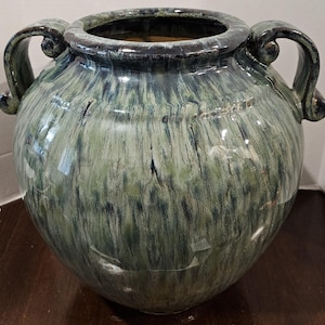 May include: A large, round ceramic vase with two curved handles. The vase has a glossy finish with a blend of green and blue hues, creating a marbled effect. The rim and handles are a darker shade of green.