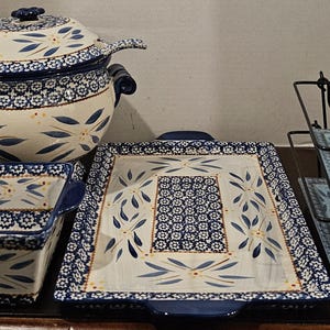May include: A collection of ceramic serving dishes with a blue and white floral pattern. Includes a lidded soup tureen, a square baking dish, a rectangular serving platter, and a tiered serving rack with matching plates.
