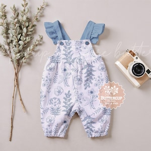 Peut inclure: Salopette bébé blanche avec un motif floral bleu et des bretelles à volants bleus. La salopette a une poche sur le devant et est faite d'un tissu doux et confortable.