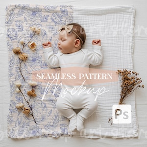 May include: A white baby onesie with a floral pattern on a white muslin blanket. The onesie has a seamless pattern mockup text on it. The baby is wearing a brown headband.