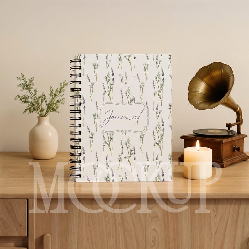 May include: A spiral-bound journal with a lavender floral pattern and the word "Journal" in script. A vintage gramophone, a lit candle, and a small vase with greenery are on a wooden surface.