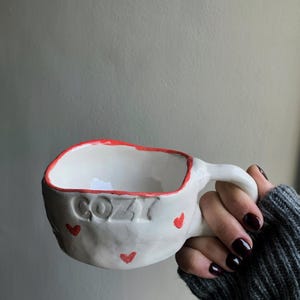 Taza de cerámica sencilla hecha a mano con pequeños corazones rojos