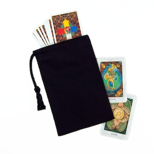 May include: A black drawstring bag with a deck of tarot cards. The cards have colorful, detailed illustrations. The bag is made of a dark fabric and has a black drawstring closure. The cards are white with colorful images.