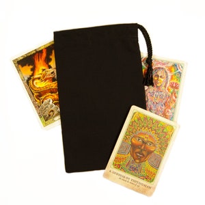 May include: A black drawstring bag with a tassel, partially obscuring several tarot cards. The cards feature colorful illustrations, including a dragon, a figure with a lotus flower, and a card labeled "Goddess of Teotihuacan".
