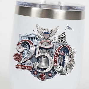 Op de afbeelding: Witte ge&iuml;soleerde beker met een zilveren rand en deksel. De beker heeft een patriottisch ontwerp met de tekst "250 AMERICA 2026" en afbeeldingen van de Amerikaanse vlag, het Vrijheidsbeeld en de Liberty Bell.