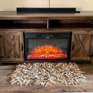 Puede incluir: Un mueble de entretenimiento de madera con una chimenea eléctrica incorporada. La chimenea muestra un efecto de llama realista. El mueble tiene dos puertas con un diseño en X y un estante encima de la chimenea. Una alfombra decorativa está frente al mueble.