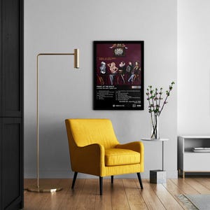 Op de afbeelding: Een zwart ingelijste poster met een bandfoto en de tekst "Panic at the Disco" en "A Fever You Can't Sweat Out". De poster hangt aan een witte muur boven een gele fauteuil.