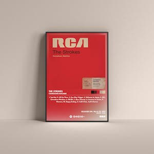 May include: A framed poster for The Strokes' "Comedown Machine" album. The poster has a red backdrop with white text, including the band's name and album title. The tracklist and release date are also displayed.
