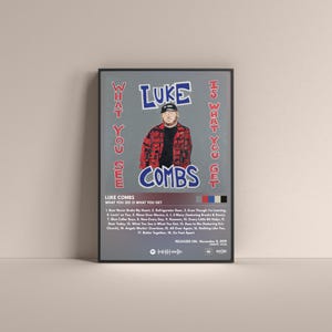 May include: A framed poster featuring Luke Combs' album "What You See Is What You Get." The poster has a gray background with the album title and artist's name in blue and white text. A photo of Luke Combs is in the center.