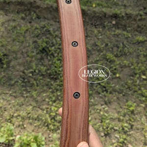 May include: Close-up of a knife handle with a brown textured grip and black screws. The blade's metal top is visible. The text "LEGION BLADEWORKS" is printed on the handle.