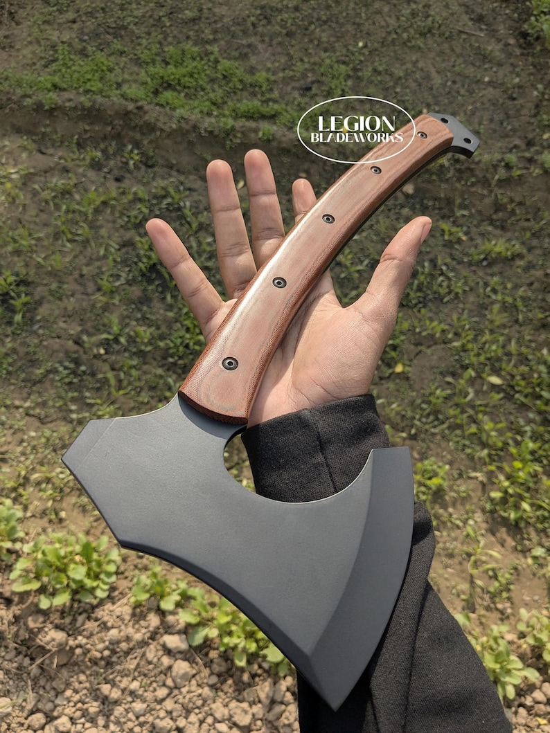 May include: Axe with a dark gray blade and a wooden handle. The handle is light brown with dark rivets. The axe has a curved blade and a hammer on the back. The text "LEGION BLADEWORKS" is in a white oval.