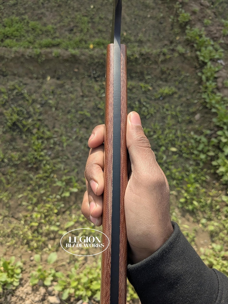 May include: A close-up of a knife with a dark blade and a brown handle. The handle has a black stripe down the center. The text "LEGION BLZ DEWORKS" is visible on the handle.