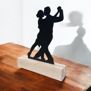 Könnte beinhalten: Schwarze Silhouette eines Paares, das auf einem Holzsockel tanzt. Die Silhouette zeigt einen Mann und eine Frau in einer Tango-Pose.