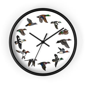 May include: A black framed clock with a white face and a design of 12 ducks flying in a circle around the clock hands.