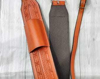 May include: A set of brown leather horse tack components, including a wide, embossed strap with a pocket, a narrower strap, and a long strap with a metal clasp. The leather has decorative stitching and silver-colored metal hardware.