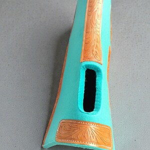 May include: A turquoise-colored leather boot with a cutout and decorative brown leather accents. The brown leather features an embossed floral design. The boot is likely for a horse or equestrian use.