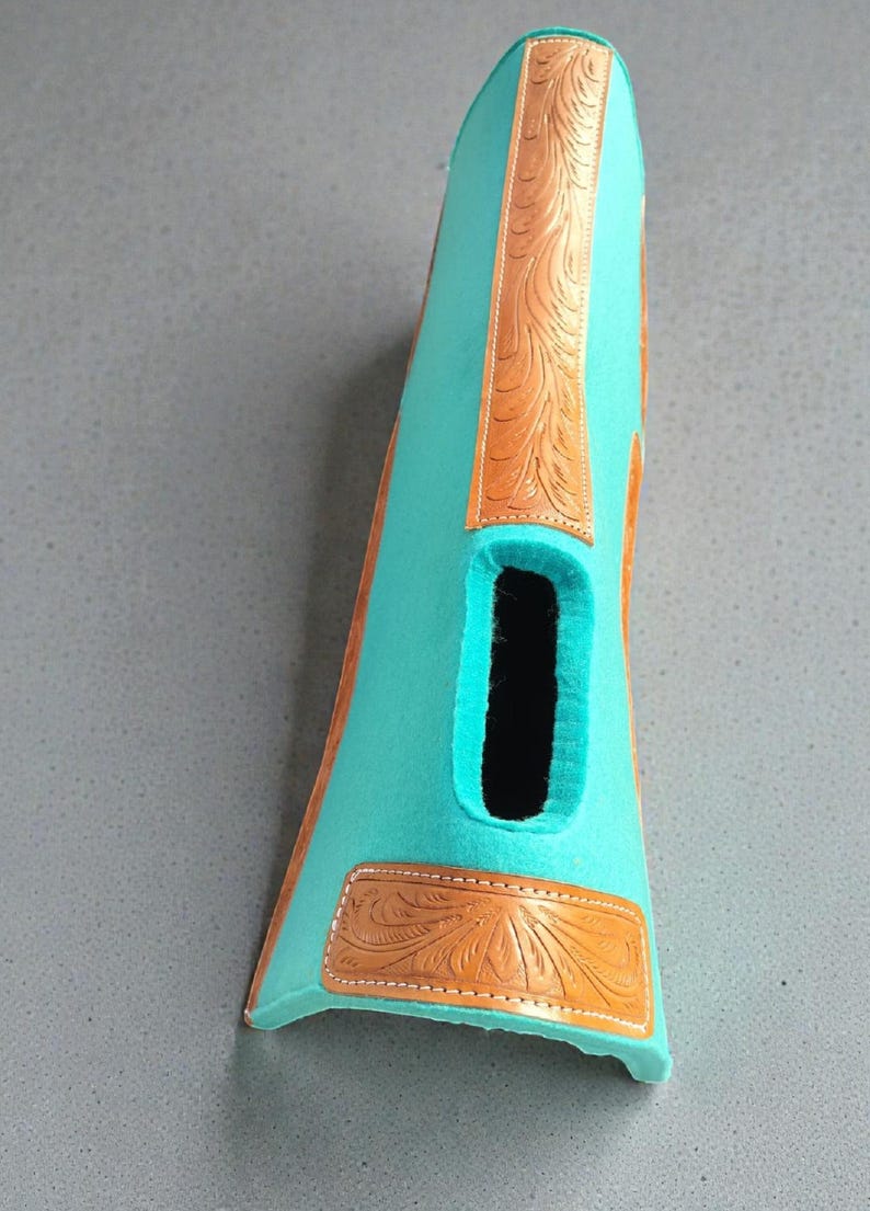 May include: A turquoise-colored leather boot with a cutout and decorative brown leather accents. The brown leather features an embossed floral design. The boot is likely for a horse or equestrian use.