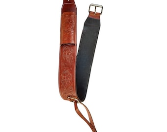 May include: A pair of brown leather saddle straps with floral tooling. The straps have silver-colored buckles and a dark brown backing. A smaller strap with a buckle hangs from the bottom.