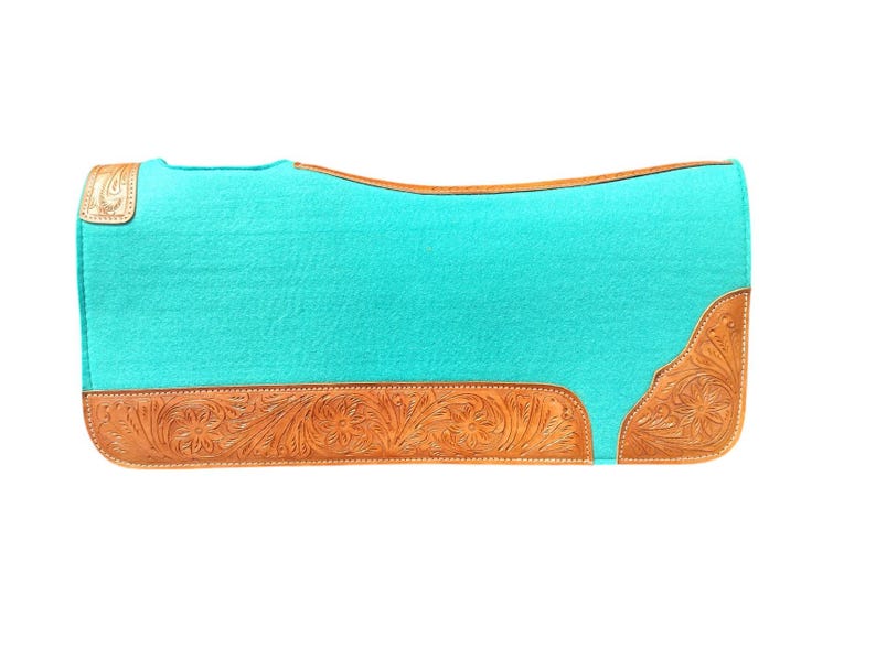 May include: A turquoise saddle pad with a rectangular shape. The pad features a light brown, tooled leather border with floral designs. The leather accents are on the bottom and corners of the pad.