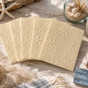 May include: A set of five cream-colored rectangular cards featuring an embossed design of starfish, seashells, and coral patterns. The cards are arranged in a fan shape, displaying a consistent textured surface with detailed marine life imagery.