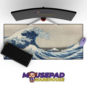 Puede incluir: Alfombrilla de ratón rectangular con la obra de arte "La Gran Ola de Kanagawa" en azul y blanco. Un teclado negro y un ratón morado están a ambos lados. Un monitor curvo está encima. El logotipo de Mousepad Warehouse es visible.