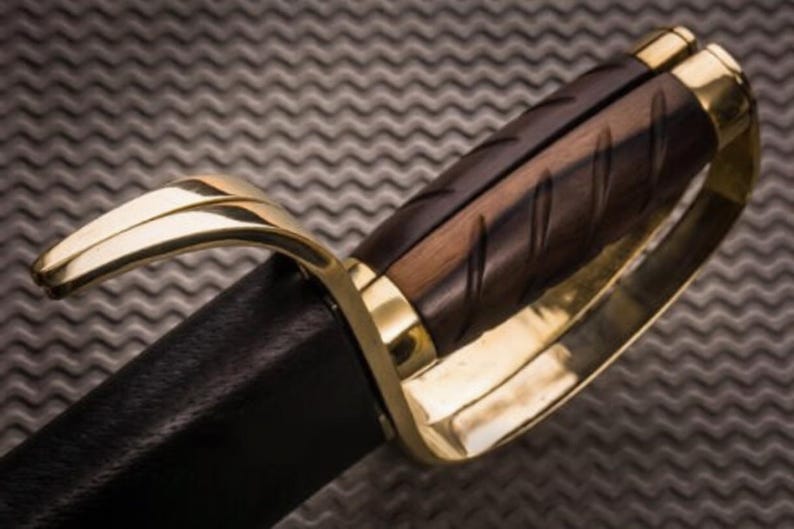 K&ouml;nnte beinhalten: Nahaufnahme eines Schwertgriffs. Der Griff ist aus dunkelbraunem Holz mit geschnitzten Rillen, umrahmt von goldfarbenem Metall. Die Klinge ist in schwarzes Leder geh&uuml;llt. Das Design deutet auf ein historisches oder Fantasy-Thema hin.