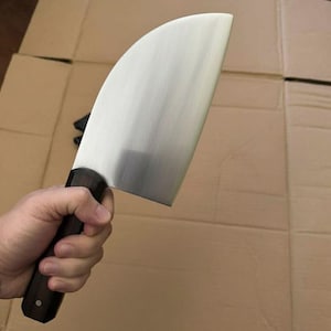 May include: A large, stainless steel cleaver with a curved blade and a dark wooden handle. The blade has a polished finish, and the handle is dark brown with a rounded shape. The cleaver is designed for chopping and cutting.