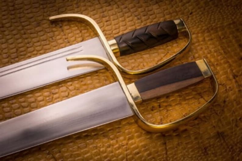 K&ouml;nnte beinhalten: Zwei Wing Chun Schwerter mit polierten Stahlklingen und messingfarbenen Griffen. Die Griffe sind aus dunkelbraunem Holz. Die Schwerter werden auf einer strukturierten, braunen Oberfl&auml;che pr&auml;sentiert.