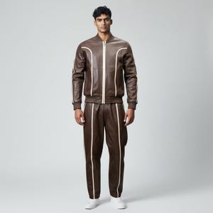 Può includere: Un completo giacca bomber e pantaloni in pelle marrone. La giacca ha una chiusura con zip e strisce bianche sulle maniche. I pantaloni hanno strisce bianche sui lati. L'outfit è indossato con scarpe da ginnastica bianche.