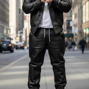 Pu&ograve; includere: Giacca in pelle nera con collo e pantaloni in pelle nera abbinati. L'outfit &egrave; abbinato a scarpe da ginnastica bianche. La giacca ha una chiusura con bottoni e polsini a coste. I pantaloni hanno una vita con coulisse.