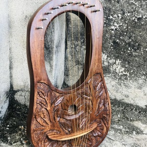 May include: A wooden lyre with a carved floral design and gold strings. The lyre has a rounded body and a sound hole in the center.