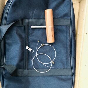 May include: A black nylon carrying case with a zipper closure, a wooden tuning key, and two sets of strings.
