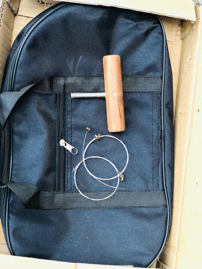 May include: A black nylon carrying case with a zipper closure, a wooden tuning key, and two sets of strings.