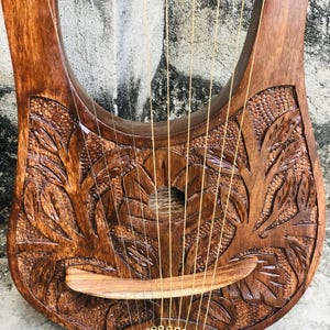 May include: A wooden lyre with a carved floral design and gold tuning pegs. The lyre has 10 strings and a wooden bridge.