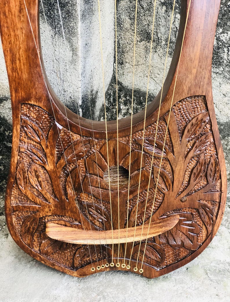 May include: A wooden lyre with a carved floral design and gold tuning pegs. The lyre has 10 strings and a wooden bridge.