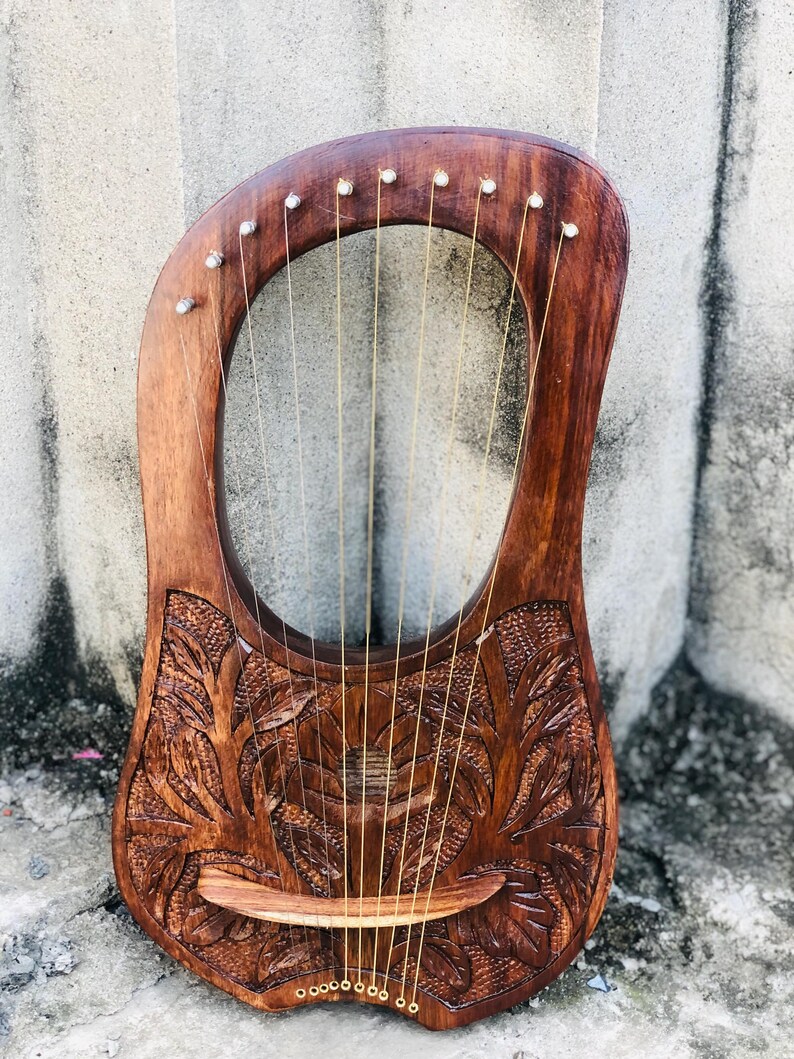 May include: A wooden lyre with a carved floral design. The lyre has 10 strings and a wooden bridge.