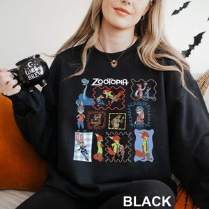 Puede incluir: Sudadera negra de cuello redondo con un gr&aacute;fico colorido de personajes de la pel&iacute;cula animada "Zootopia". El dise&ntilde;o incluye el t&iacute;tulo de la pel&iacute;cula y varias ilustraciones de personajes dentro de marcos decorativos. La palabra "BLACK" est&aacute; impresa en la parte inferior.