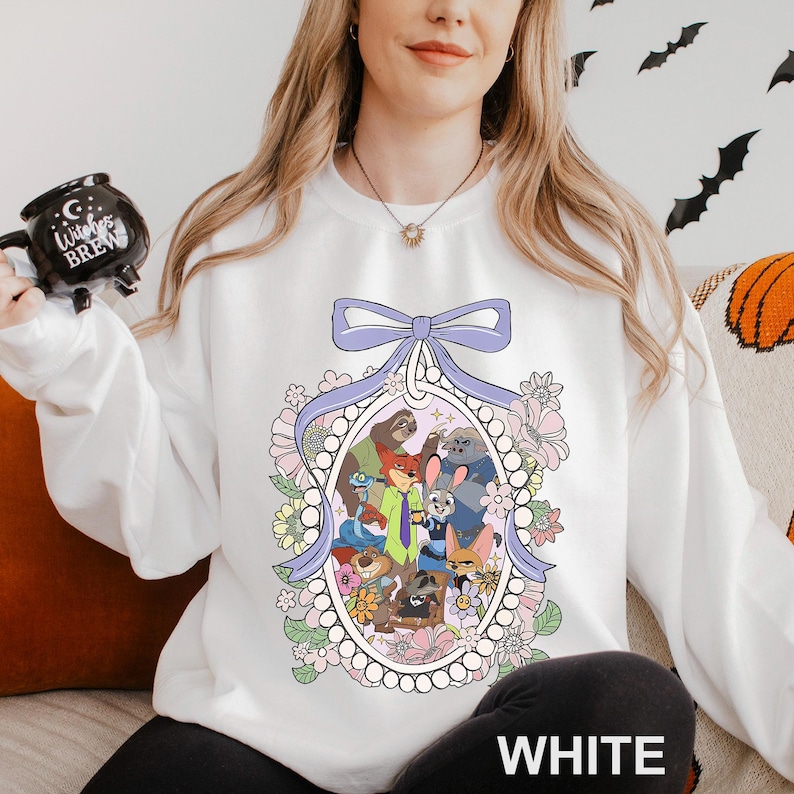 May include: White sweatshirt with a cartoon illustration of animal characters in a floral oval frame, with a lavender bow. The word "WHITE" is printed at the bottom. The sweatshirt is a casual style.
