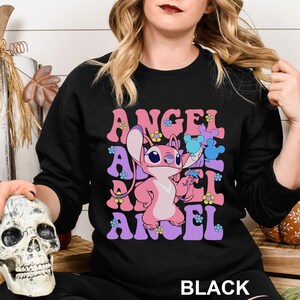 Peut inclure: Sweat-shirt noir avec le mot "ANGEL" en lettres roses et violettes avec des accents floraux. Un personnage de dessin anim&eacute; rose est au centre. Le mot "BLACK" est en bas.