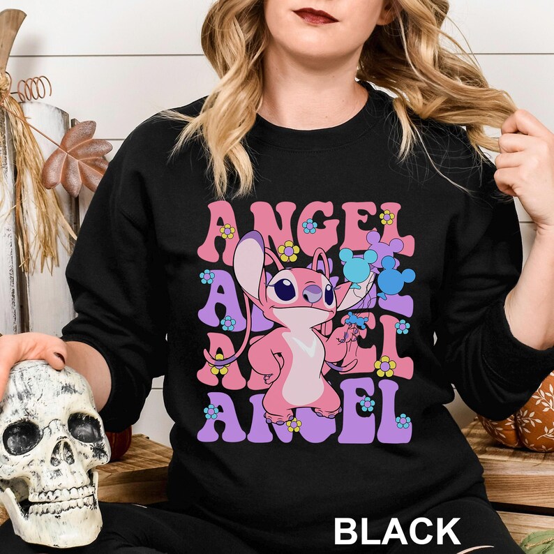 Peut inclure: Sweat-shirt noir avec le mot "ANGEL" en lettres roses et violettes avec des accents floraux. Un personnage de dessin anim&eacute; rose est au centre. Le mot "BLACK" est en bas.