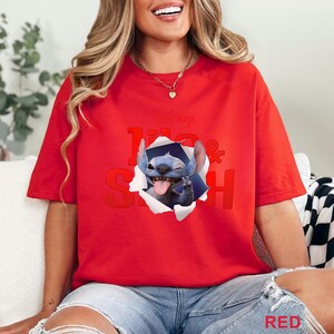 May include: Red t-shirt featuring a graphic of Stitch from Disney's Lilo & Stitch, bursting through a torn paper effect. The text "Lilo & Stitch" is printed in red. The word "RED" is printed in the bottom right corner.