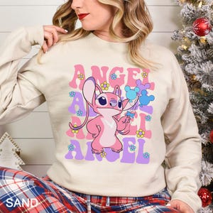 Peut inclure: Un sweat-shirt couleur sable avec un personnage de dessin anim&eacute; rose et le mot "ANGEL" en lettres roses et violettes. Le motif comprend des fleurs et des ballons bleus. Le sweat-shirt a des manches longues.
