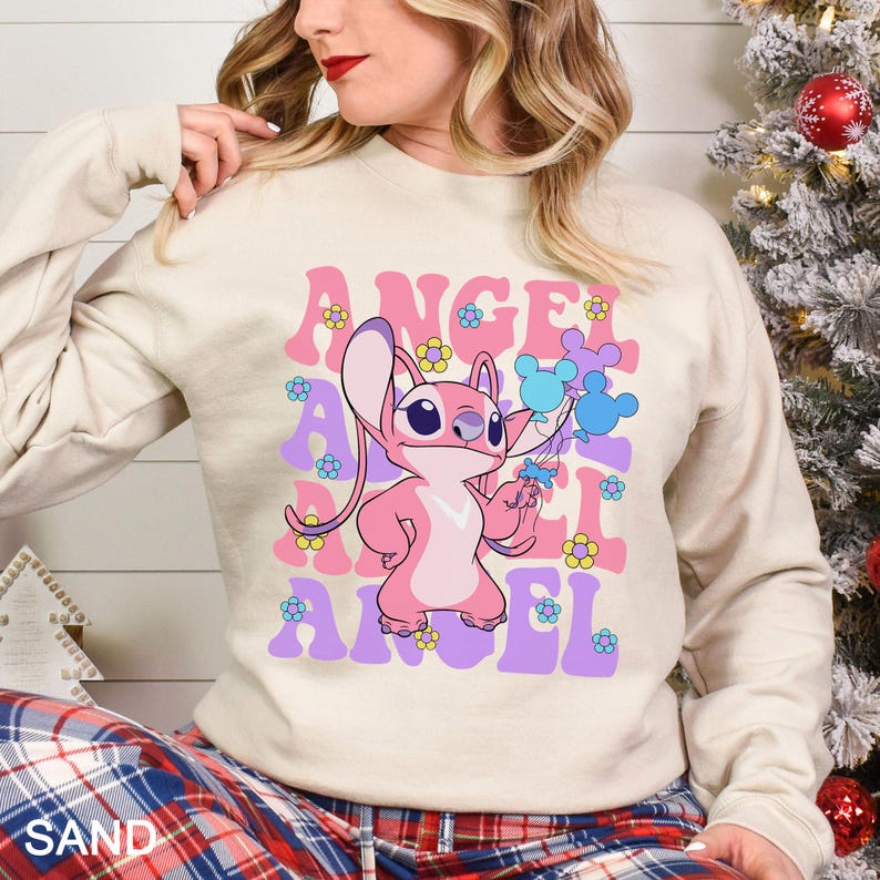 Peut inclure: Un sweat-shirt couleur sable avec un personnage de dessin anim&eacute; rose et le mot "ANGEL" en lettres roses et violettes. Le motif comprend des fleurs et des ballons bleus. Le sweat-shirt a des manches longues.